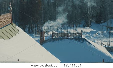 Roof of traditional snow-covered russian palace - terem in a forest.. Smoke coming from the chimney. Top view