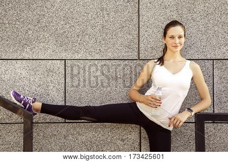 Fitness beautiful woman with freckles on her face drinking water and sweating after exercising in city. Female athlete after work out. looking at camera and smilling.