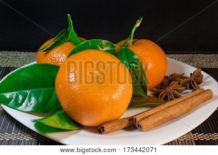 Tangerines on the plate with spice, black background.