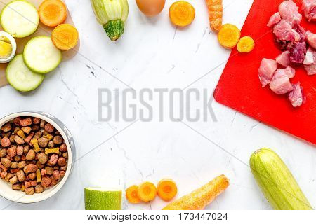 Bowl of dry dogfood with fresh carrot, courgette and cut meat on white table background top view mock-up