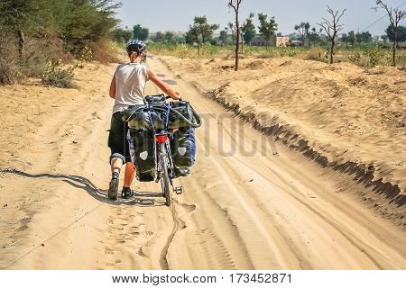 Woman pushing her bicycle through the sand while cycling through remote desert road in Rajasthan India