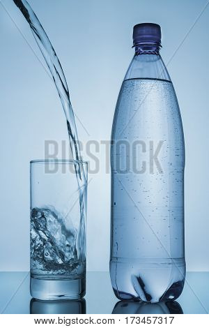 water poured into glass and bottle on blue background