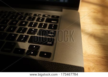 Laptop computer keyboard on sunshine on wooden background.