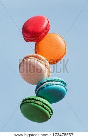 Different types of macaroons in motion falling on light blue background. Sweet and colorful french macaroons falling or flying in motion. 
