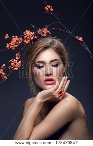 Beautiful young woman with make-up and loose hairdo holding artificial sakura branch with orange flowers. Beauty shot on dark background. Copy space.