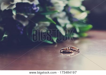 Beautiful wedding rings lie on a wooden surface against the background of a bouquet of flowers