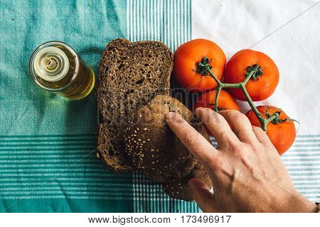 Hand over on Olive oil tomato and slides of brown bread on tablecloth. Top view