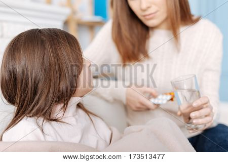 Feeling ill. Sick little girl sititng on the couch while her mother giving pills and lookign at her