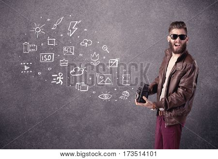 An elegant hipster guy trying to use a vintage camera with camera settings icons drawn on wall, like flash, white balace or ISO value concept
