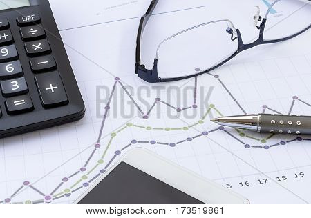 calculator glasses pen mobile phone and financial chart business work station with paperwork is on the desk finance and business concept