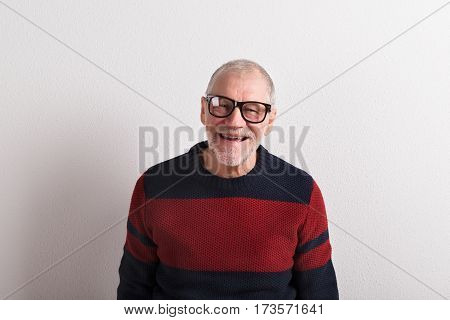 Handsome senior man in red and blue sweater and black eyeglasses, smiling. Studio shot against white wall.