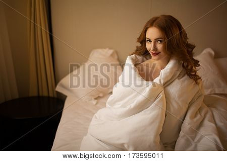 Red-haired girl covered herself with a blanket in the bed