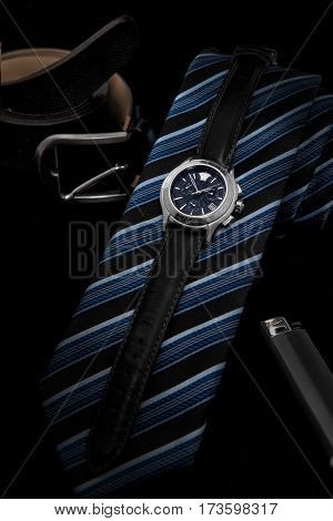 Men's wrist watch on a black strap in the set with a tie and a lighter. On a black background