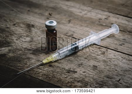 Medical injection syringe with vial on wooden background.