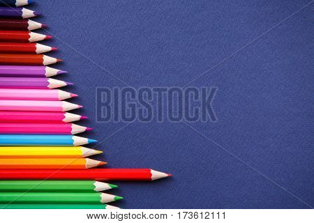 one red pencil standing out from the series of colorful pencils. on blue background. Sign symbol idea concept of leadership, opposition, confrontation. Standoff of the individual to society