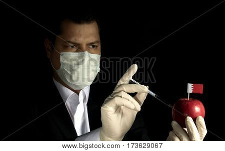 Young Businessman Injecting Chemicals Into An Apple With Bahraini Flag On Black Background