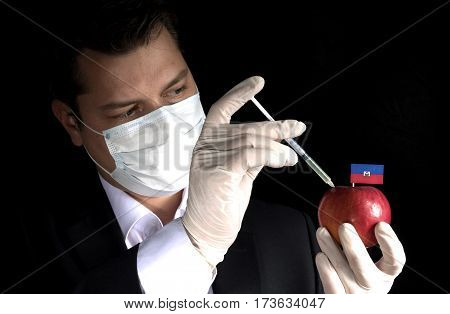 Young Businessman Injecting Chemicals Into An Apple With Haitian Flag On Black Background