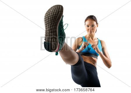 A young female dressed in gym clothes performing a martial arts kick on isolated white background
