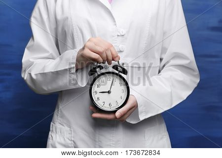Doctor holding alarm clock on color background