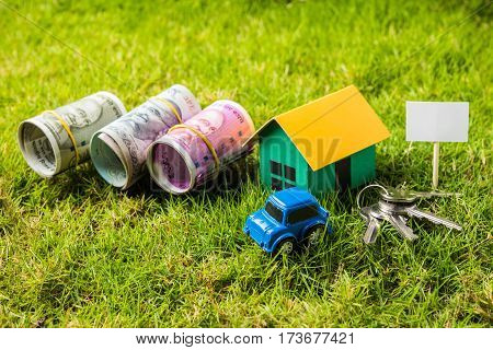 indian currency notes of rupees 100, 500 and 2000 in roll or stack with small home model, keys, toy car and calculator with blank board over green grass - home buying and finance concept in India