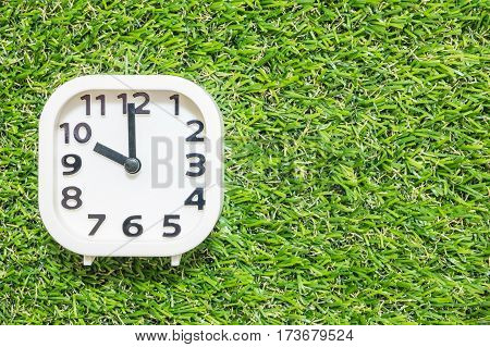 Closeup white clock for decorate in 10 o'clock on green artificial grass floor textured background with copy space