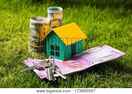 indian currency notes of rupees 100, 500 and 2000 in roll or stack with small home model, keys, toy car and calculator with blank board over green grass - home buying and finance concept in India