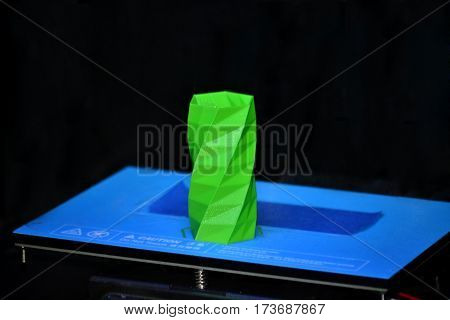 The object printed 3D printer on a blue and black background in the 3D printer. Automatic three dimensional 3d printer performs plastic green colors modeling in laboratory.