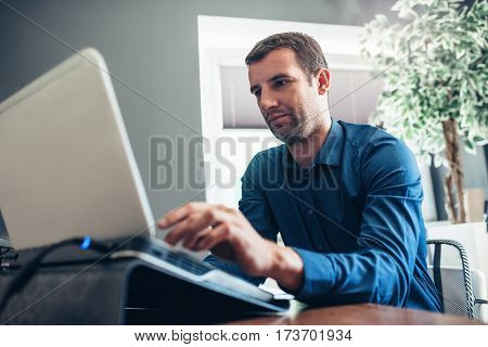 Confident and successful young businessman focused on work while sitting at a desk in an office using a laptop