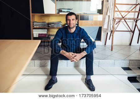Portrait of a confident and successful young businessman smiling while sitting on the floor in a large work studio