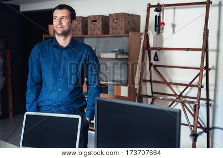 Confident and successful young businessman looking deep in thought while standing with his hands in his pockets in a large work studio