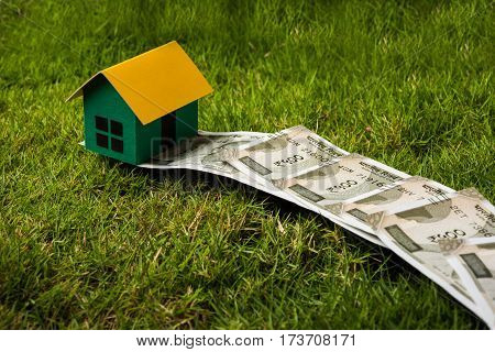 indian new currency notes of rupees 500 or 2000 forming a road to reach model house over green grass  - concept of residential property or home buying in india