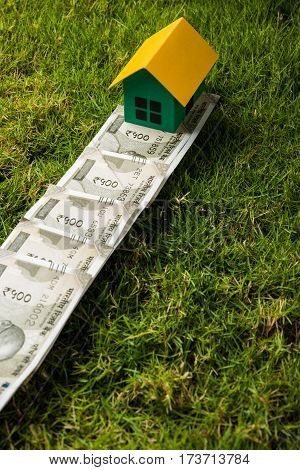 indian new currency notes of rupees 500 or 2000 forming a road to reach model house over green grass  - concept of residential property or home buying in india