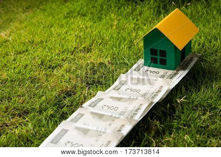 indian new currency notes of rupees 500 or 2000 forming a road to reach model house over green grass  - concept of residential property or home buying in india