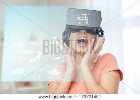 technology, augmented reality, cyberspace, e-commerce and people concept - happy amazed young woman in virtual headset or 3d glasses and headphones at home with shopping cart and menu icons projection