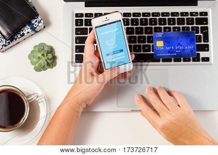 On-line shopping concept - desktop with laptop, credit card and hands holging phone with on-line shop page