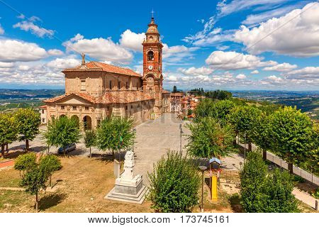 Parish church on town square under beautiful blue sky with white clouds surrounded by green trees  in small town of Diano d'Alba in Piedmont, Northern Italy.