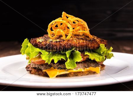 Delicious hamburger potato pancakes bun. latke burger with lettuce, cheese, tomatoes on wooden black background and white plate.