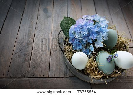 Easter eggs in a bowl with straw and blue hydrangeas on a dark wooden background