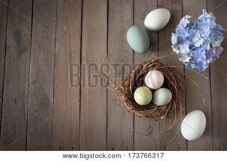 Pastel colored easter eggs in a nest with blue hydrangeas on a shabby wooden table