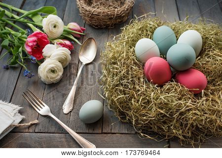 Still life with colorful easter eggs in a nest and flowers on a old shabby wooden table