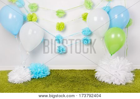 Festive background decoration for first birthday celebration or easter holiday with blue green and white paper flowers balloons fluffy rug on floor with nobody copyspace for text
