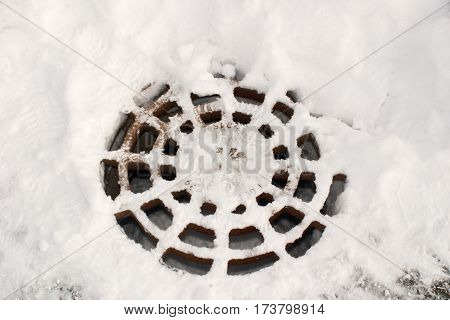 The image of a manhole, covered with snow