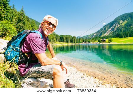 hiking senior man taking a rest by a mountain lake.