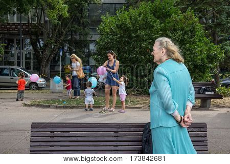 BELGRADE SERBIA - AUGUST 2 2015: Old woman looking at younger women taking care of children playing with balloons in the suburb district of Zemun