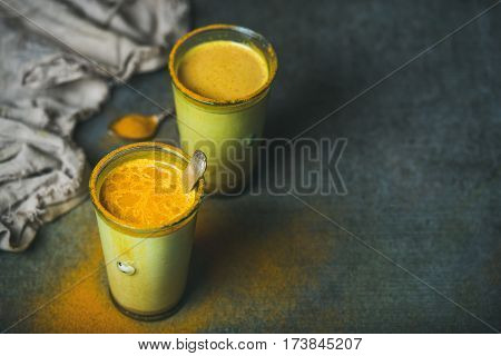 Golden milk with turmeric powder in glasses over dark grunge background, copy space. Health and energy boosting, flu remedy, natural cold fighting drink. Clean eating, detox, weight loss concept