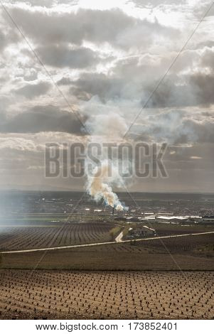 Column of smoke, expelled by an industry or farm, in the middle of a rainfed farm