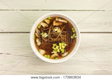 A photo of a miso soup with buckwheat soba, champignons, and green onions, shot from above on a wooden background texture with copy space