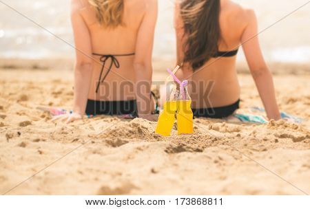 Gierlfriends drinking cold drink beverage having fun at beach party. Female babes in bikini enjoying orange water from glass boutle. summer concept