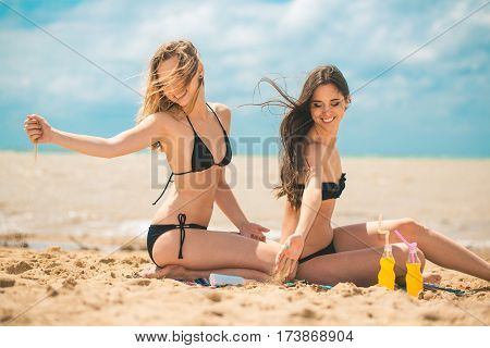 Gierlfriends drinking cold drink beverage having fun at beach party. Female babes in bikini enjoying orange water from glass boutle. summer concept