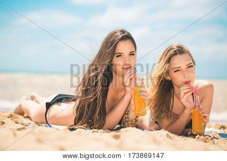 Gierlfriends drinking cold drink beverage having fun at beach party. Female babes in bikini enjoying orange water from glass boutle. summer concept